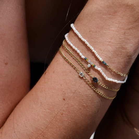 Close-up of a wrist wearing multiple gold and beaded bracelets on a dark background